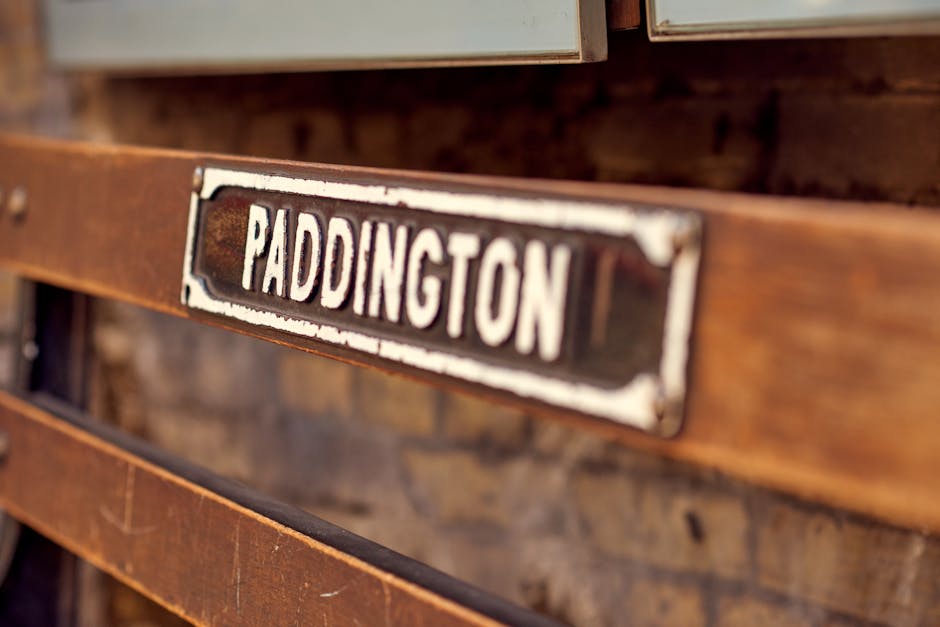 Close-up view of a vintage wooden crate with a metal label reading 'Paddington' attached to the front, featuring worn paint and rustic textures. The crate is made of aged wood with visible grain and knots, set against a blurred background of similar wooden surfaces. The lighting highlights the weathered surface and the slightly distressed metal label, emphasizing the natural and antique appearance. Paddington Carpet Cleaning, a professional cleaning service, is dedicated to surface cleaning and sanitisation, ensuring clients' spaces are thoroughly maintained and hygienic.